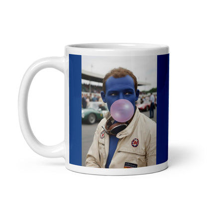 White ceramic 11oz mug with a bold blue border featuring a pop-art style portrait of Stirling Moss in a white racing suit, blue-tinted face, and blowing a pink bubblegum bubble, with a vintage racetrack scene in the background.