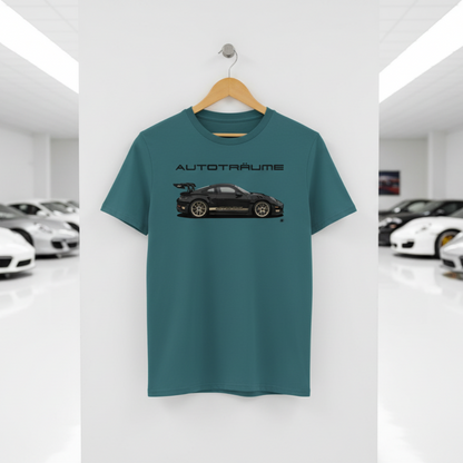 Teal AUTOTRÄUME GT3 T‑shirt with a black Porsche‑style car and gold highlights illustration hanging on a premium wooden hanger and silver wall peg against a central white wall in a bright sports car gallery, with a glossy white floor and blurred white and silver sports cars running down both sides.