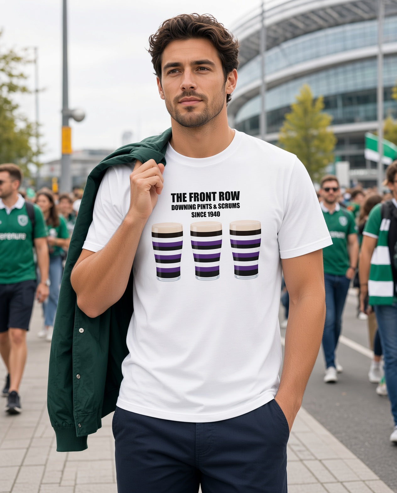 Male model wearing a white Terenure rugby t-shirt reading “The Front Row - Downing Pints & Scrums Since 1940” with three purple, black and white pint graphics, photographed in a Ireland rugby match day crowd setting