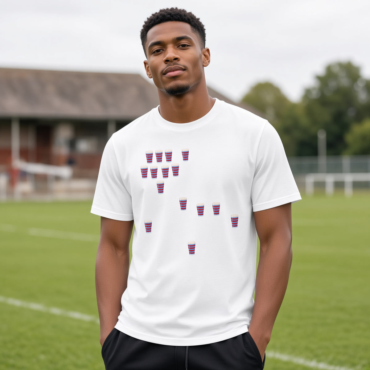 Male model wearing a white vintage Blackheath Team Pints rugby t-shirt with scattered red and light blue striped pint graphics, photographed at a rugby ground for match day supporters in South East London