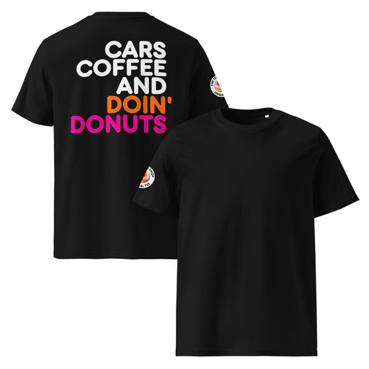 Black unisex t-shirt with a plain front, bold “Cars Coffee and Doin’ Donuts” slogan in white, orange, and pink Impact font printed large on the back, and The Tee Shop circular donut logo patch on the right sleeve. DTF printed, minimalist car meet tee for petrolheads who love a statement back print and clean style.